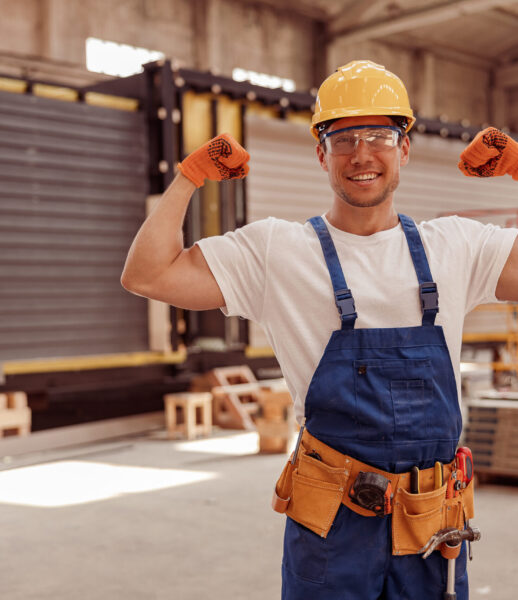 Cheerful male worker demonstrating his strong muscular arms Handsome athletic man construction worker looking at camera and smiling while showing perfect biceps muscle