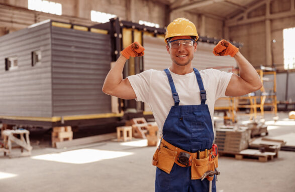 Cheerful male worker demonstrating his strong muscular arms Handsome athletic man construction worker looking at camera and smiling while showing perfect biceps muscle