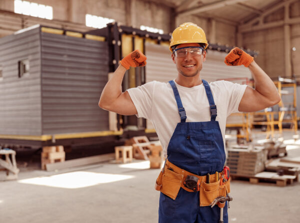 Handsome athletic man construction worker looking at camera and smiling while showing perfect biceps muscle