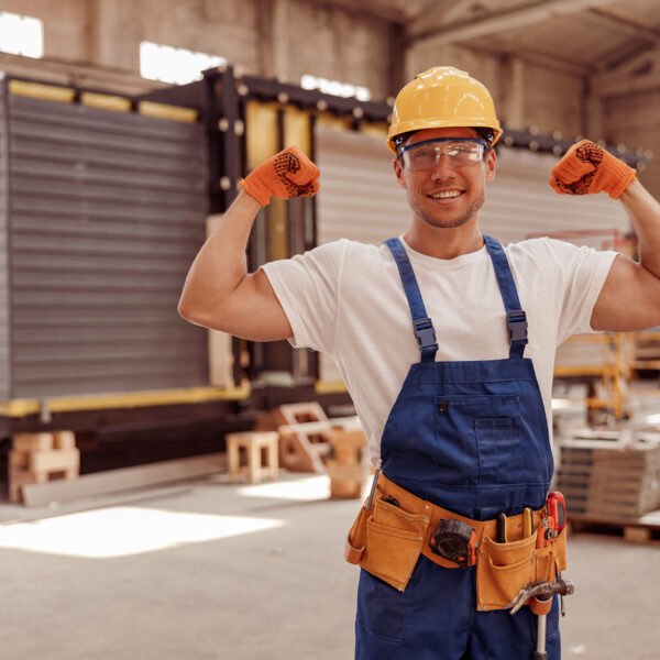 Handsome athletic man construction worker looking at camera and smiling while showing perfect biceps muscle