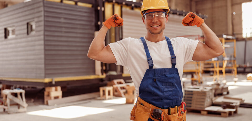 Cheerful male worker demonstrating his strong muscular arms Handsome athletic man construction worker looking at camera and smiling while showing perfect biceps muscle
